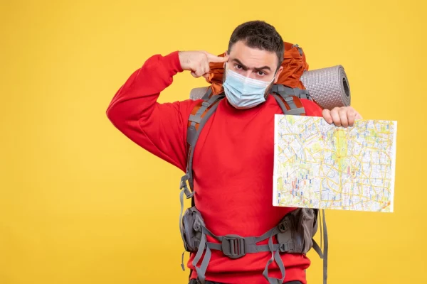 top-view-emotional-thoughtful-traveller-guy-wearing-medical-mask-with-backpack-holding-map-yellow-background